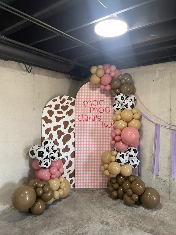 Moo Moo themed birthday arch backdrop in pink gingham and cow print with brown, tan and pink balloons