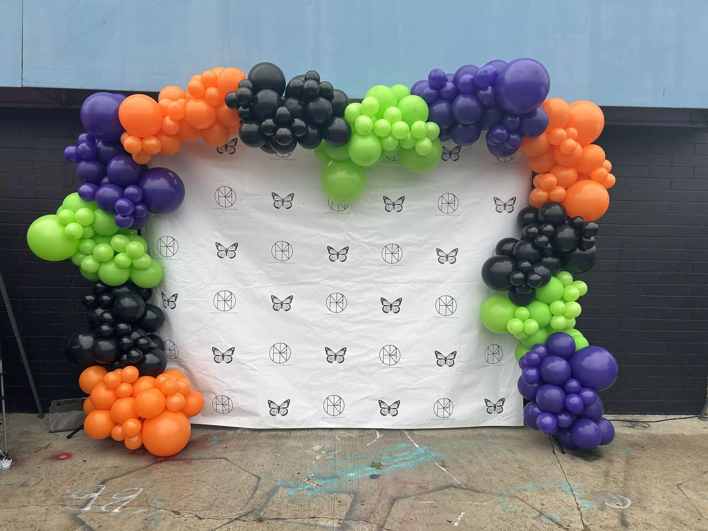 Custom balloon arch in orange, green, purple and black framing a printed photo backdrop panel