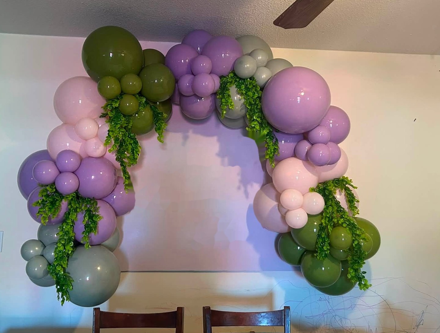 Fairy garden birthday balloon arch in sage green, olive, lavender and blush with trailing greenery over a soft lavender backdrop