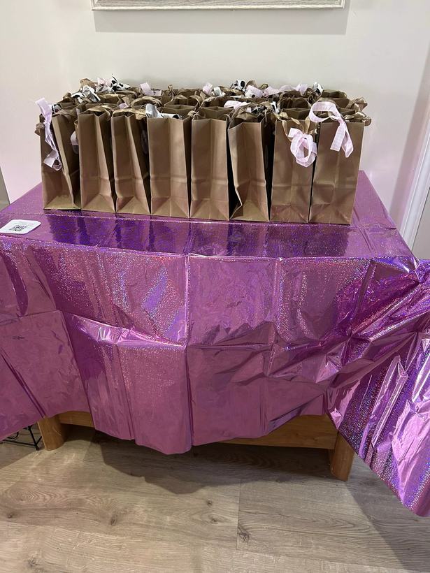 Favor table styled with a purple holographic cloth and rows of kraft paper favor bags tied with ribbon