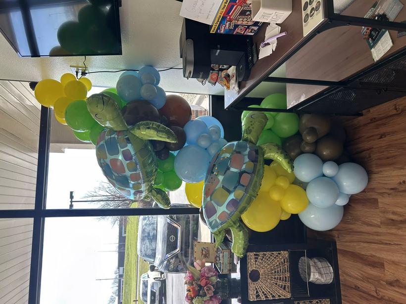 Sea turtle balloon garland installed across a storefront ceiling in blue, green and yellow