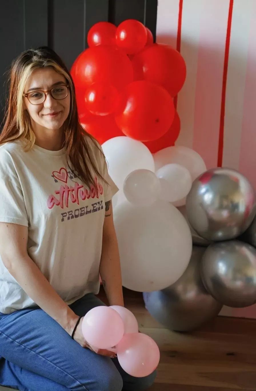 Soleil Burnett kneeling beside a red, pink, white and silver balloon garland during a Valentine's setup