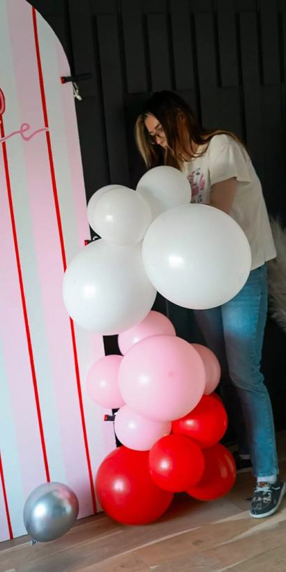 Soleil Burnett carrying a cluster of white and pink balloons into place beside a striped backdrop