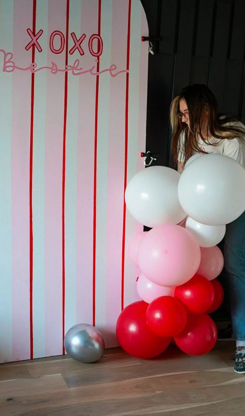 Soleil Burnett working behind a striped Valentine's backdrop while assembling a balloon column