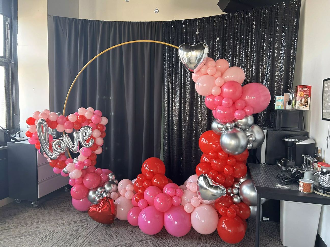 Valentine's hoop arch in red, pink and silver balloons with heart foils, built against a black drape by Burnett's Balloons by Soleil