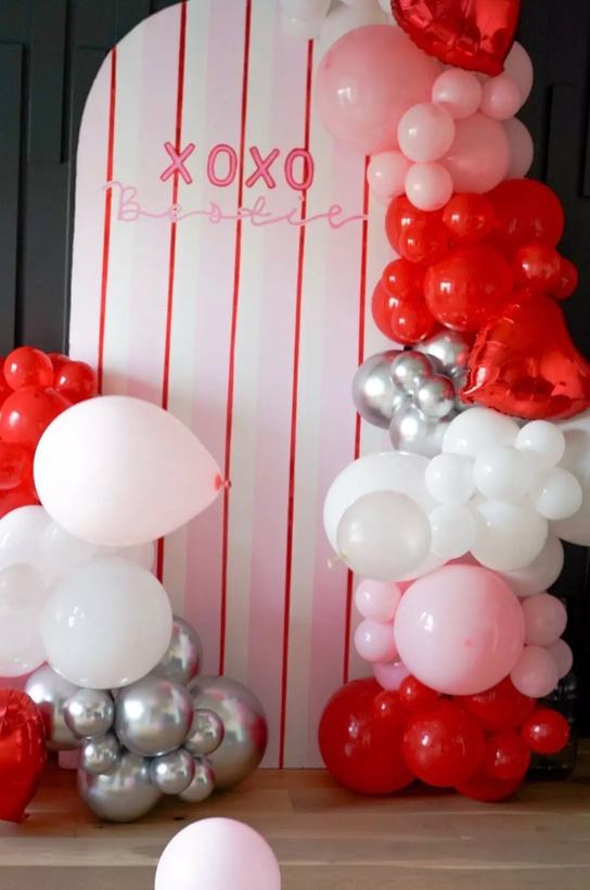 XOXO Bestie striped backdrop with red, white, pink and chrome silver balloon clusters at floor level